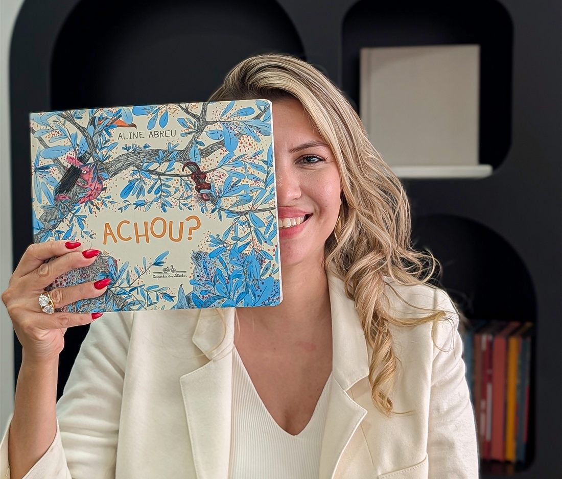 Ana Fernandes sorrindo com um livro infantil na biblioteca do Espaço NeuroLearn